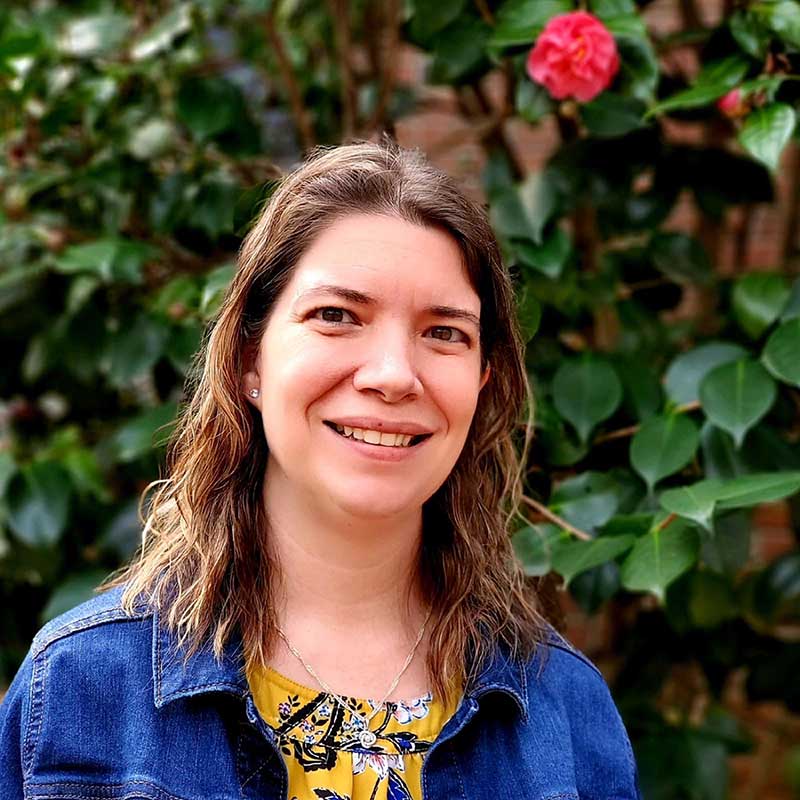Smiling woman in denim jacket beside pink flower